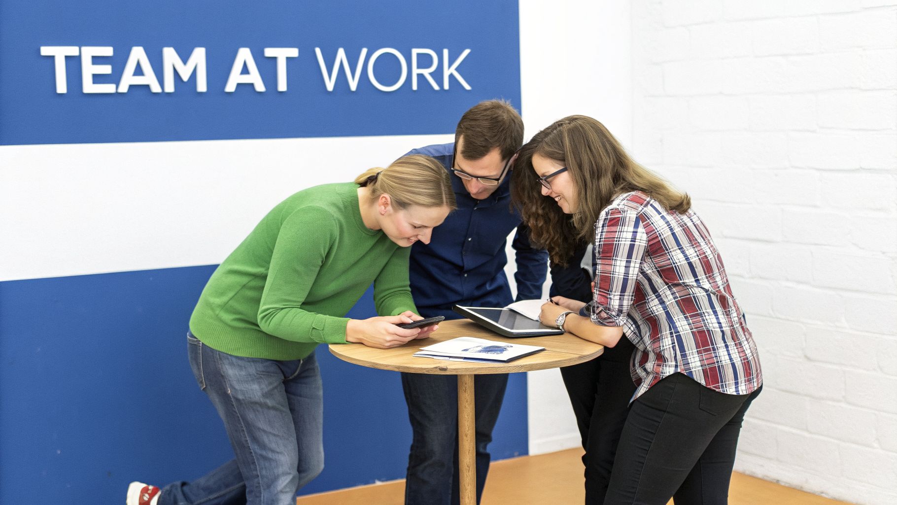 Three colleagues collaborate around a table, looking at devices and notes in an office setting.