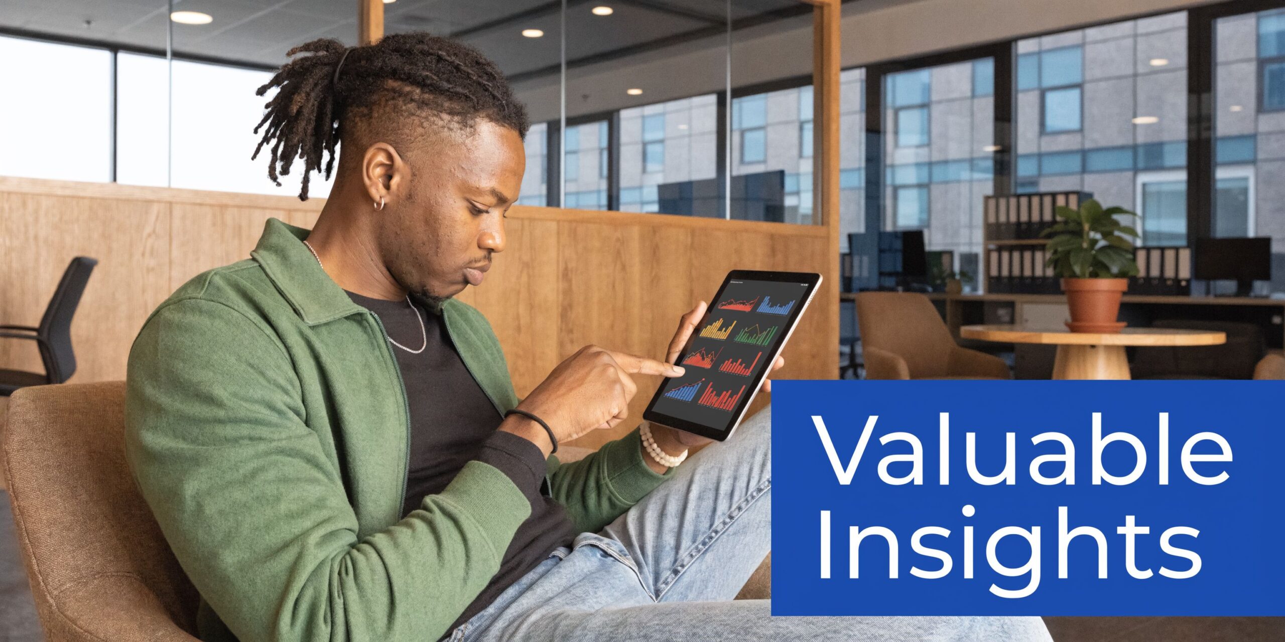 A young man sitting in an office, reviewing data visualizations on a digital tablet screen.