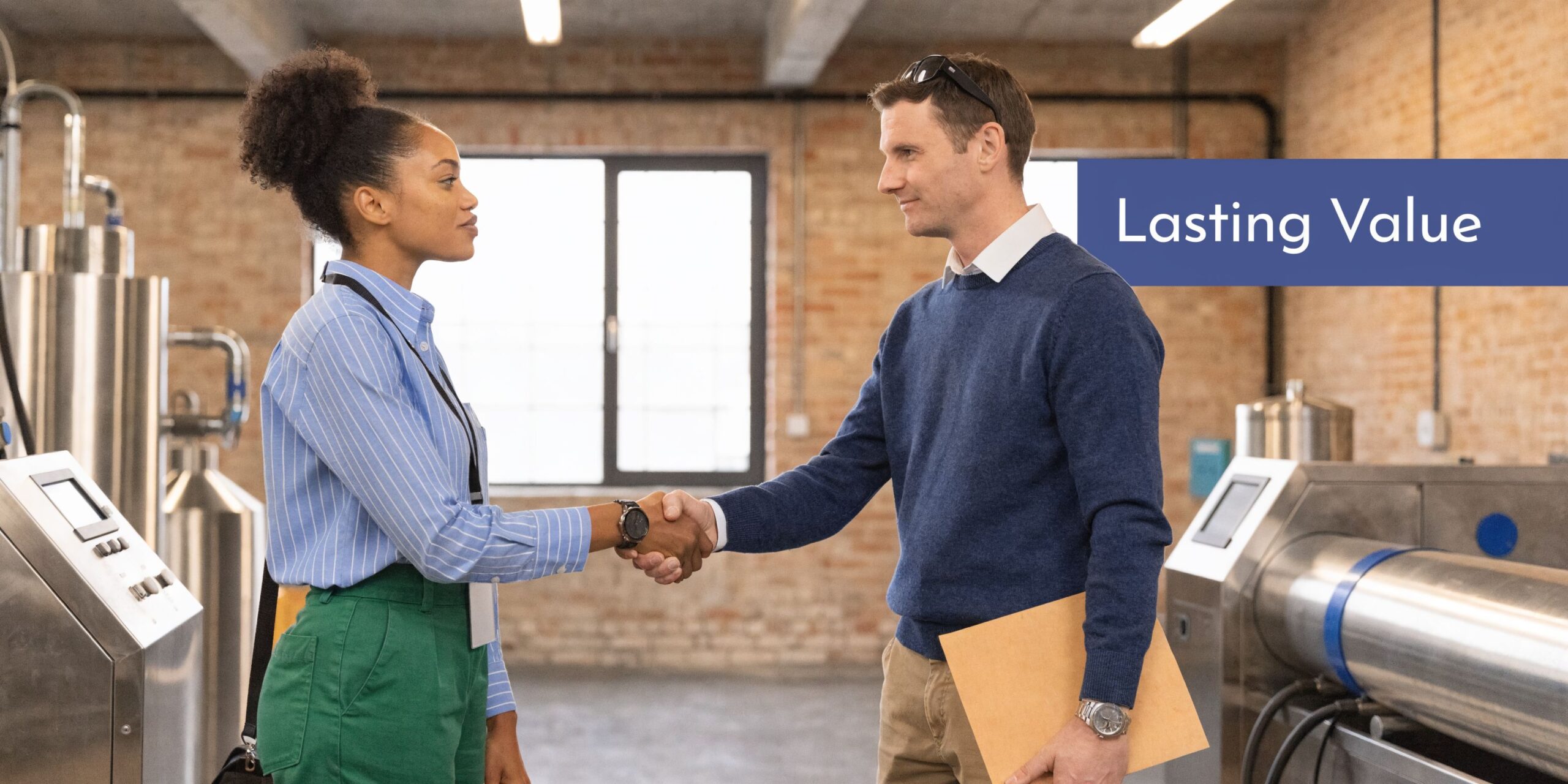 A professional woman and man shaking hands in a industrial facility, representing a successful business partnership.