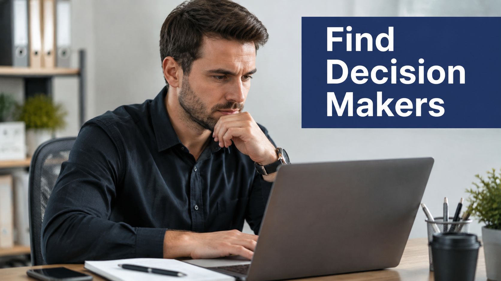 A professional man with a beard sitting at a desk looking at a laptop while searching for leads.
